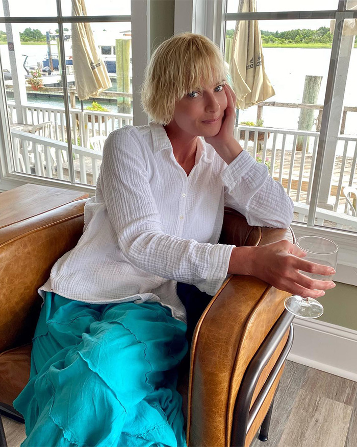 Hollywood actress smiling in a white shirt and blue skirt, relaxing by a window with a drink, reflecting on her hotel incident. Hollywood actress smiling in a white shirt and blue skirt, relaxing by a window with a drink, reflecting on her hotel incident.
