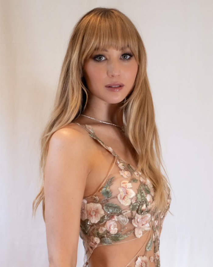 Jennifer Lawrence in a floral embroidered dress, long blonde hair with bangs. Her plastic surgery confession draws scrutiny.