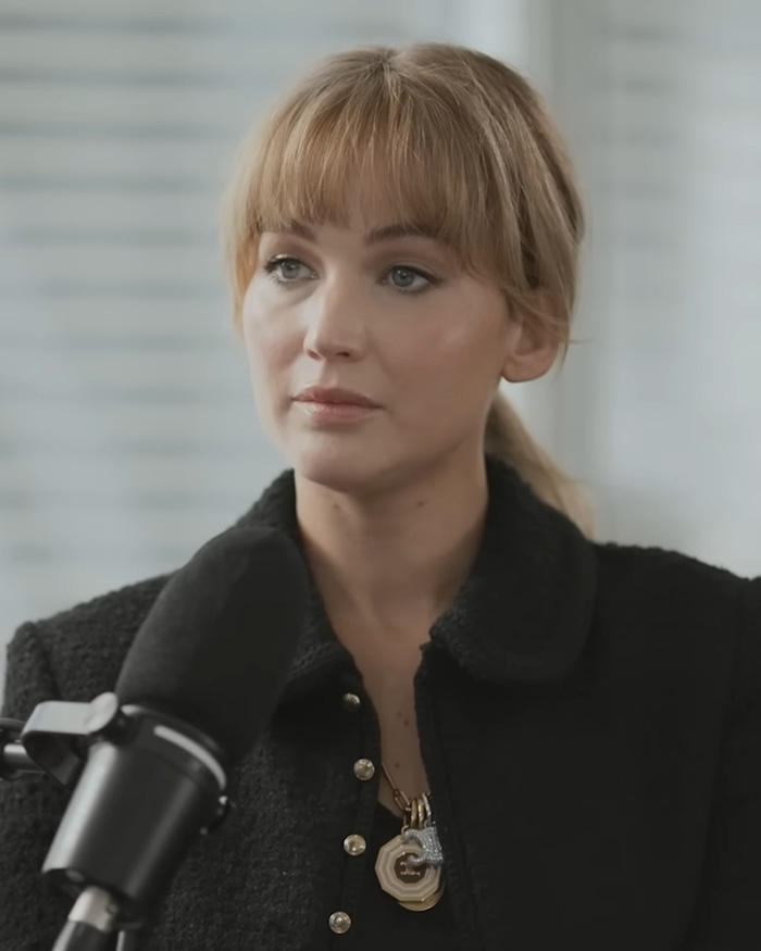 Jennifer Lawrence in a black jacket, blonde hair in a ponytail with bangs, looking serious. Her plastic surgery confession sparks scrutiny.
