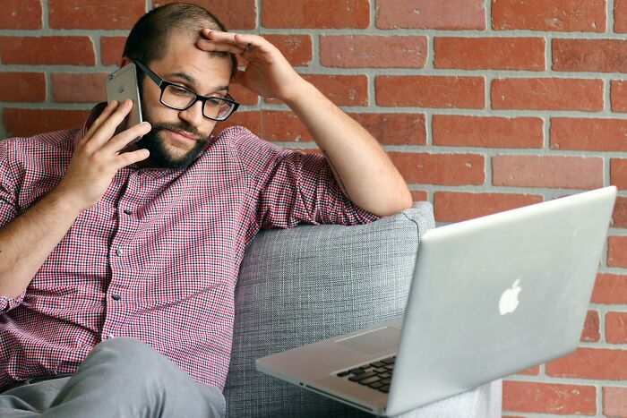 A stressed man on a phone call while looking at his laptop, highlighting challenges in the job market.