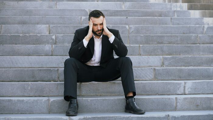 A stressed man in a suit sitting on stairs, reflecting the struggles of being unemployed in today's job market