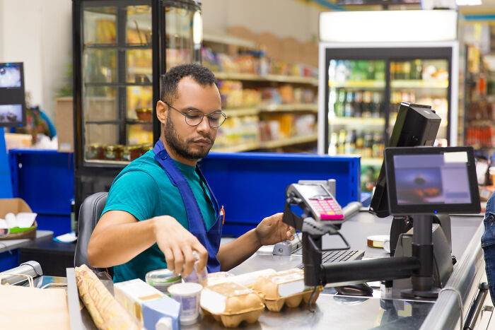 A grocery store cashier working at the checkout counter, showing options in a tough job market