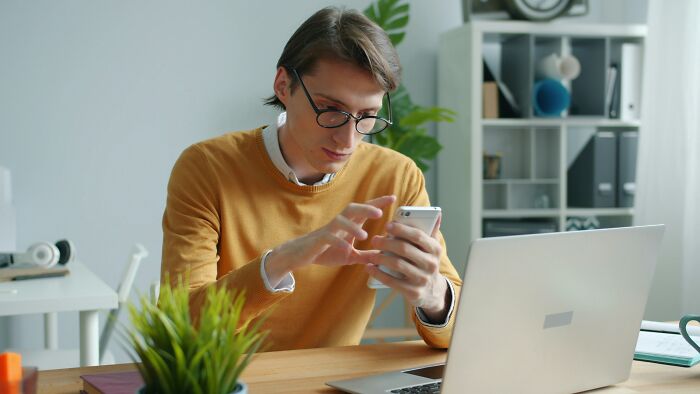 A man in a yellow sweater looking at his phone, representing people affected by the changing job market