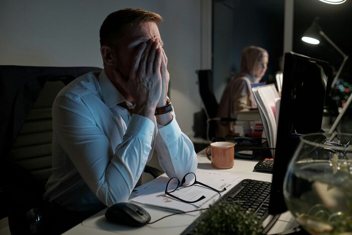 An exhausted worker covering his face at his desk at night, illustrating a tough job market.