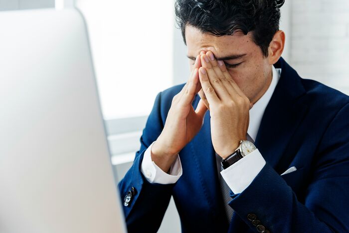 A stressed businessman covering his eyes at his computer, highlighting a difficult job market.
