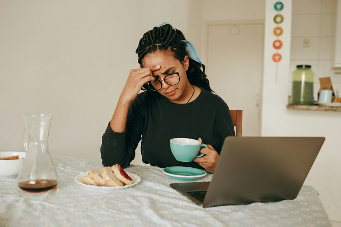 A stressed woman sitting in her kitchen with a laptop, reflecting on the challenges of being unemployed