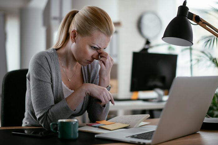 Tired woman at desk rubbing her eyes, feeling the strain of looking for work in a tough job market.