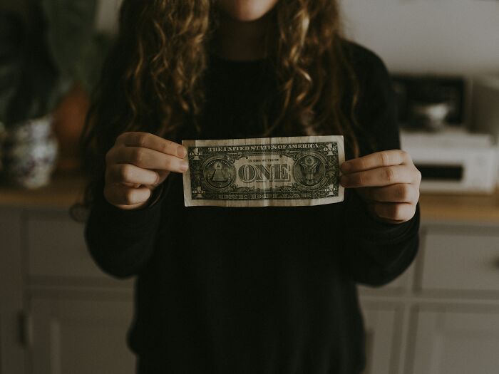 A person holding a one-dollar bill, illustrating the financial strain in a difficult job market.