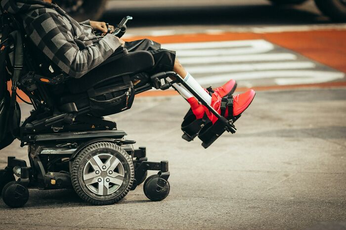 A person in a motorized wheelchair with red shoes navigates a street, symbolizing the journey of going no contact with a parent.