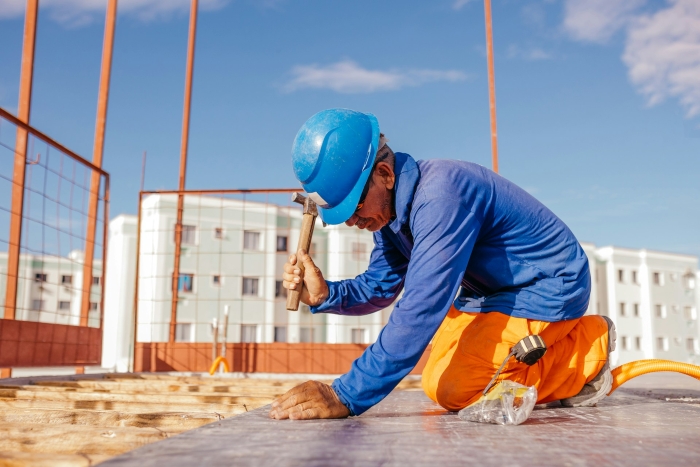 A blue-collar husband in a hard hat hammers nails into wood under a clear blue sky, illustrating a new trend. A blue-collar husband in a hard hat hammers nails into wood under a clear blue sky, illustrating a new trend.