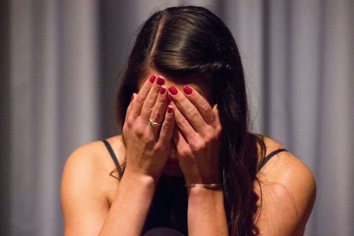 Young woman with red nails covering her face, experiencing pain from going no contact with a parent.