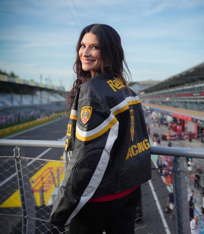 Laura Pausini in a racing jacket at a track, smiling at the camera, showing Instagram versus reality.