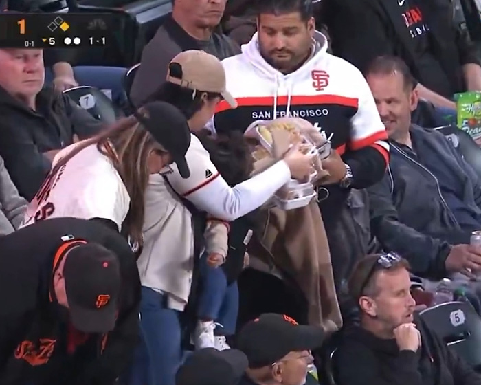 A woman in a baseball jersey holding stacked food containers, highlighting treatment of wife at game. A woman in a baseball jersey holding stacked food containers, highlighting treatment of wife at game.