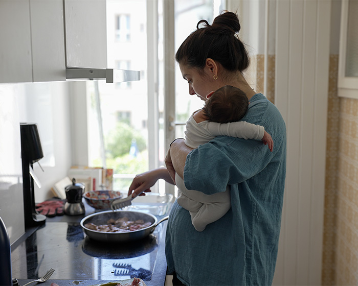 A mother cooking in the kitchen while holding her baby, showing the treatment of wife by husband A mother cooking in the kitchen while holding her baby, showing the treatment of wife by husband