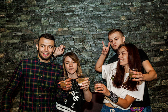 Four young adults, two men and two women, holding drinks in a bar-like setting. Four young adults, two men and two women, holding drinks in a bar-like setting.