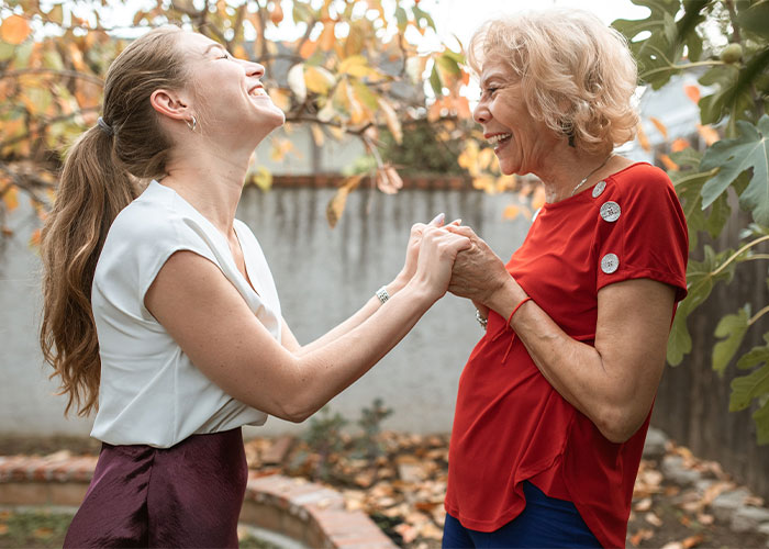 Two women holding hands and smiling outdoors representing mother and wife relationship