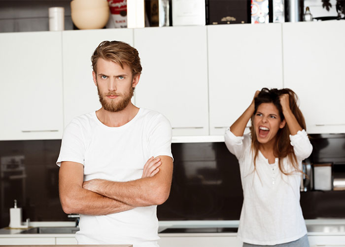 Man appears upset while woman shouts in kitchen over relationship conflict