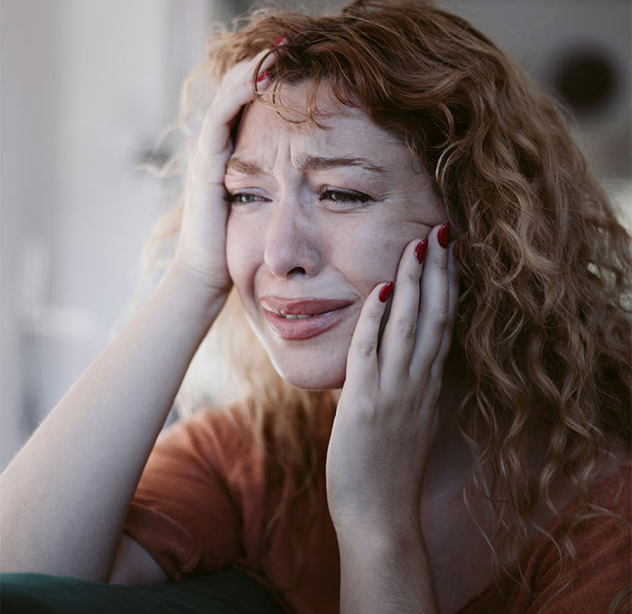 Woman with curly hair crying and holding her face showing emotional distress