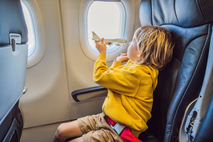 A young boy playing with a toy plane by the window, a common passenger activity flight attendants might find annoying.