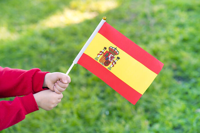 Child holding a small Spanish flag with blurred greenery background