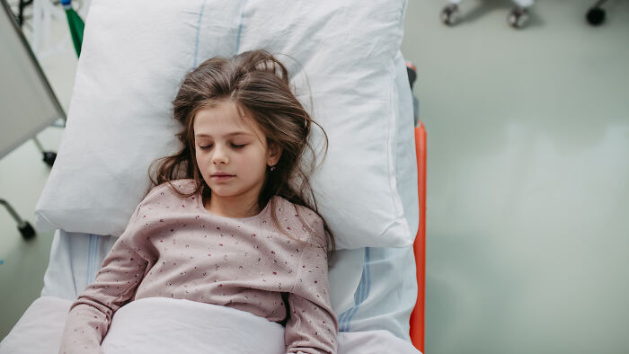 A young girl asleep in a hospital bed, reflecting pain reactions.