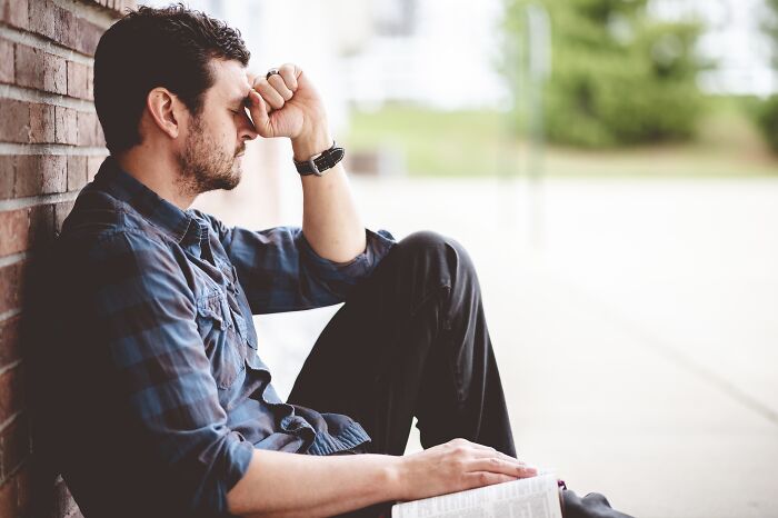 A man sitting with his hand on his forehead, reflecting on past marriages and the impact of divorce.