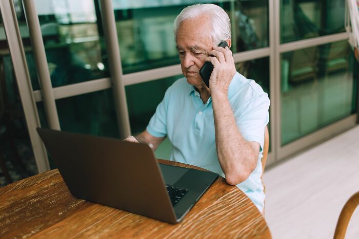 Elderly man using a laptop and talking on the phone after over 20 years in a marriage.