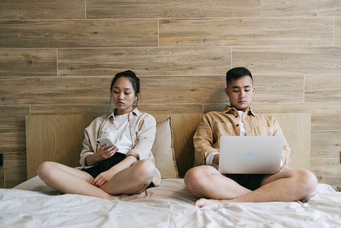 A couple sits in bed, disconnected by their devices, symbolizing shifts in marriage after 20 years.