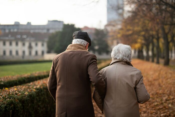 An elderly couple walks hand-in-hand in a park, representing the duration of marriage over 20 years.