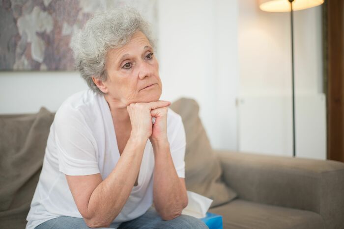 A pensive elderly woman sits on a couch, reflecting on her marriage after more than 20 years.