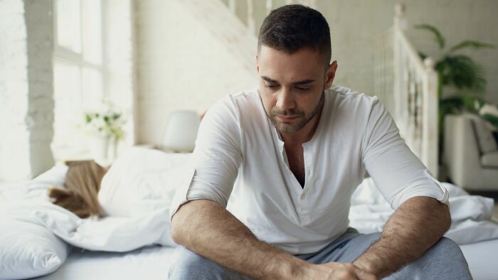 Man sitting on a bed, looking upset after over 20 years in a marriage.
