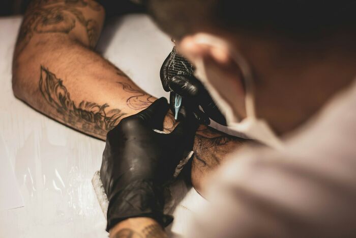 Wildly stupid things people said, a close-up of a tattoo artist in black gloves tattooing an arm.