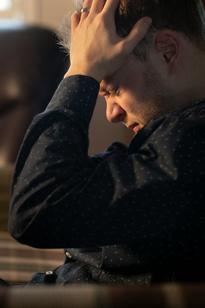 Man holds head in distress, considering dinner options, perhaps anticipating hot tea from a table nearby.