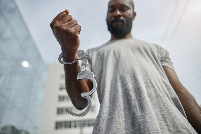 A man in handcuffs, showing one of the dumb ways people ruin their lives.