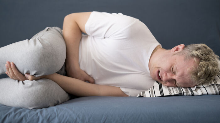 A man lying on a bed, clutching his stomach in pain, depicting extreme illness and sickness.