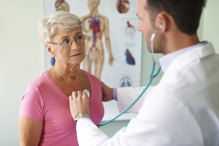 A medical worker listening to a senior patient's heartbeat with a stethoscope.