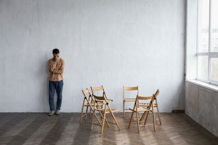 A man standing alone against a wall near chairs, depicting mental health patient stories in therapy