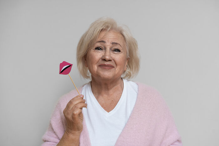 A senior woman holding a paper lips prop on a stick next to her face.