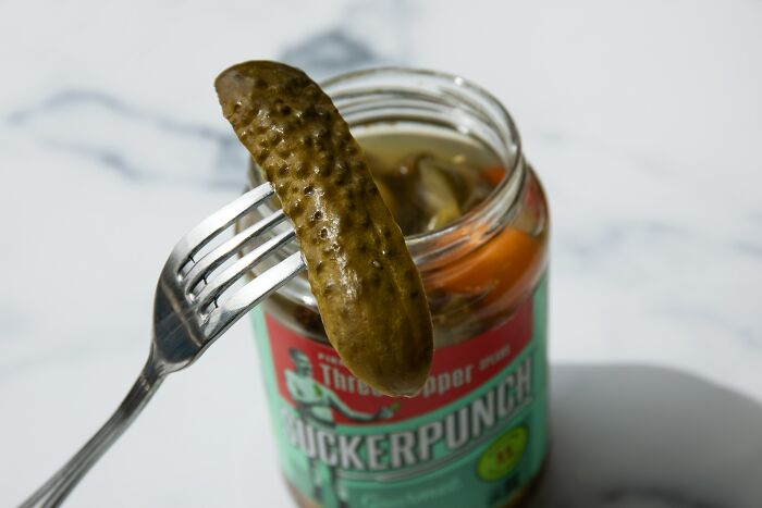 A pickle held on a fork above a jar for patient stories