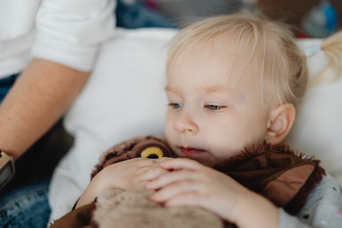 A young patient resting with a teddy bear, whose patient stories inspire medical workers.