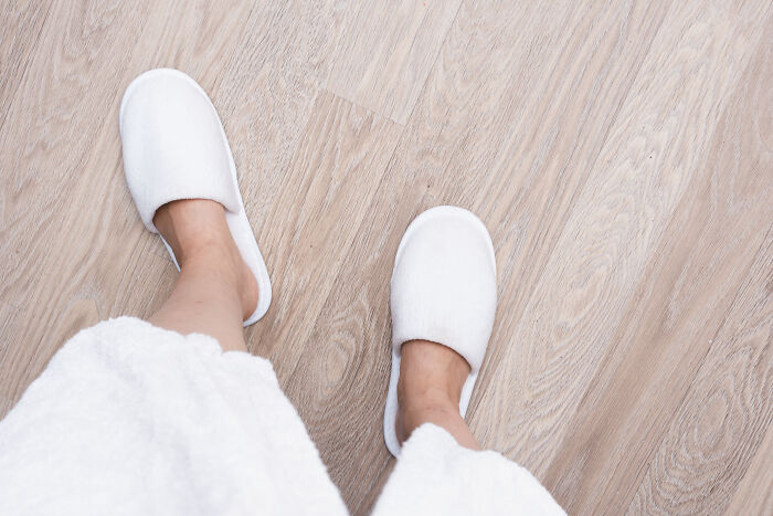 A patient wearing white slippers and a robe standing on a wooden floor, sharing patient stories