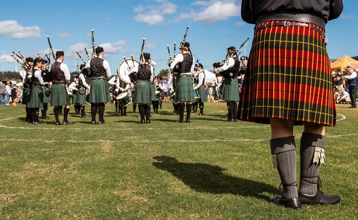 A bagpipe band in kilts, performing outdoors where people gather to share patient stories.
