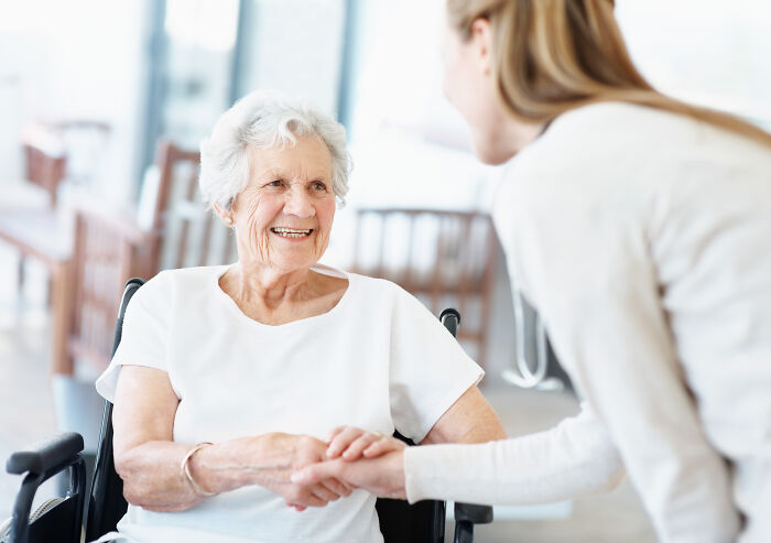 A friendly medical worker holds the hand of an elderly patient in a wheelchair, sharing sweet stories.