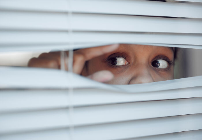 A pair of eyes peeking curiously through white window blinds, representing medical workers observing patients