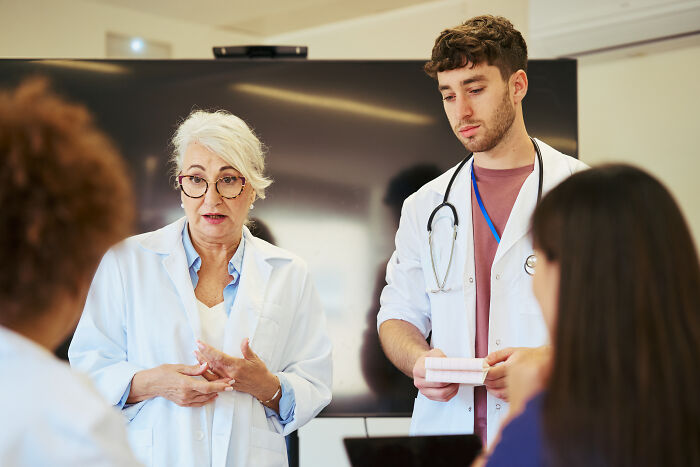 Medical professionals in lab coats, one speaking, in a meeting where someone might overhear something they weren't meant to hear.