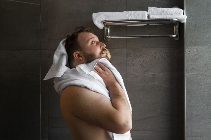 Man drying off with white towel in a bathroom with towels hanging