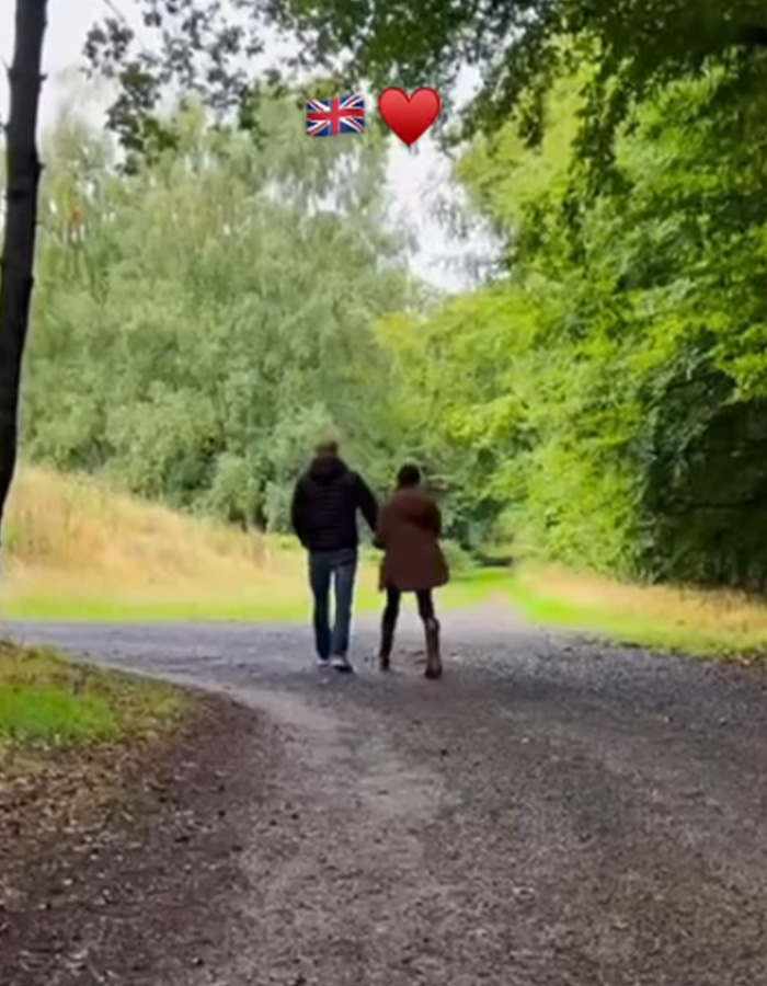 Meghan Markle and Prince Harry walk hand-in-hand down a tree-lined path. A Union Jack and heart emoji float above. Meghan Markle and Prince Harry walk hand-in-hand down a tree-lined path. A Union Jack and heart emoji float above.