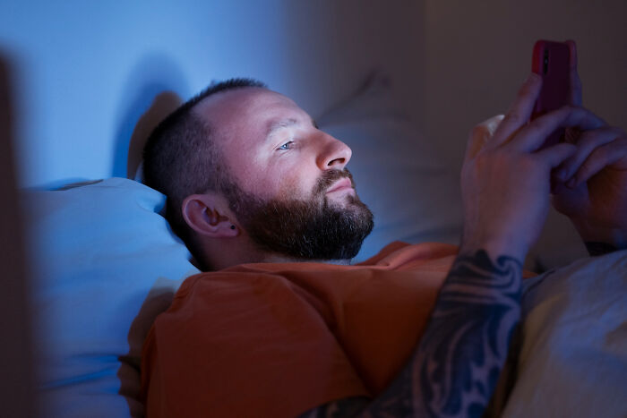 Man lying in bed using phone at night showing toxic relationship behaviors