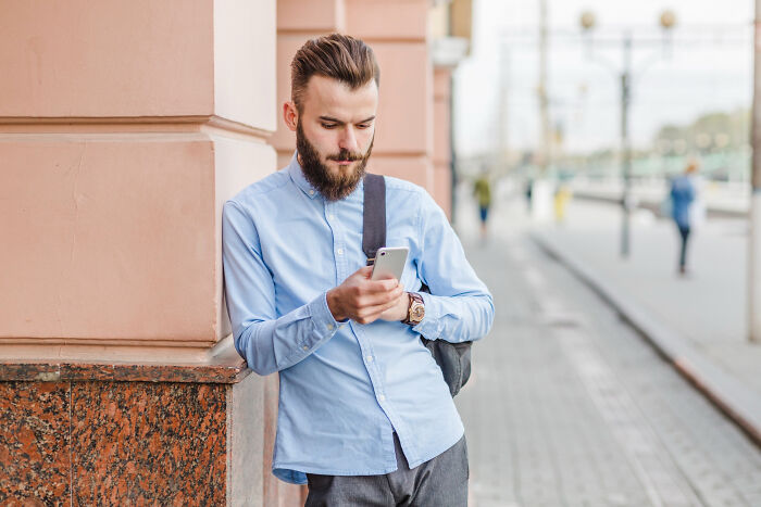 Young man checking phone outside urban building, symbolizing ex-boyfriend toxicity