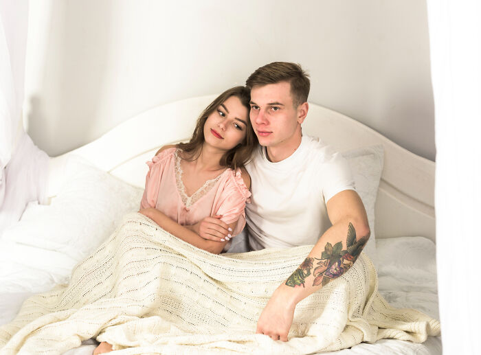 Young couple sitting close in bed wrapped in a blanket showing intimacy